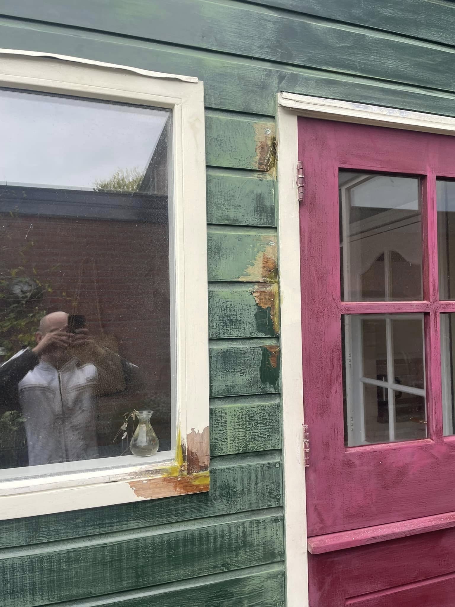 Tijdens het werk: raamkozijn en betimmering naast de bordeauxrode deur, met gele gevulde plekken waar houtrot is hersteld. (Facebook, 16 oktober 2024)