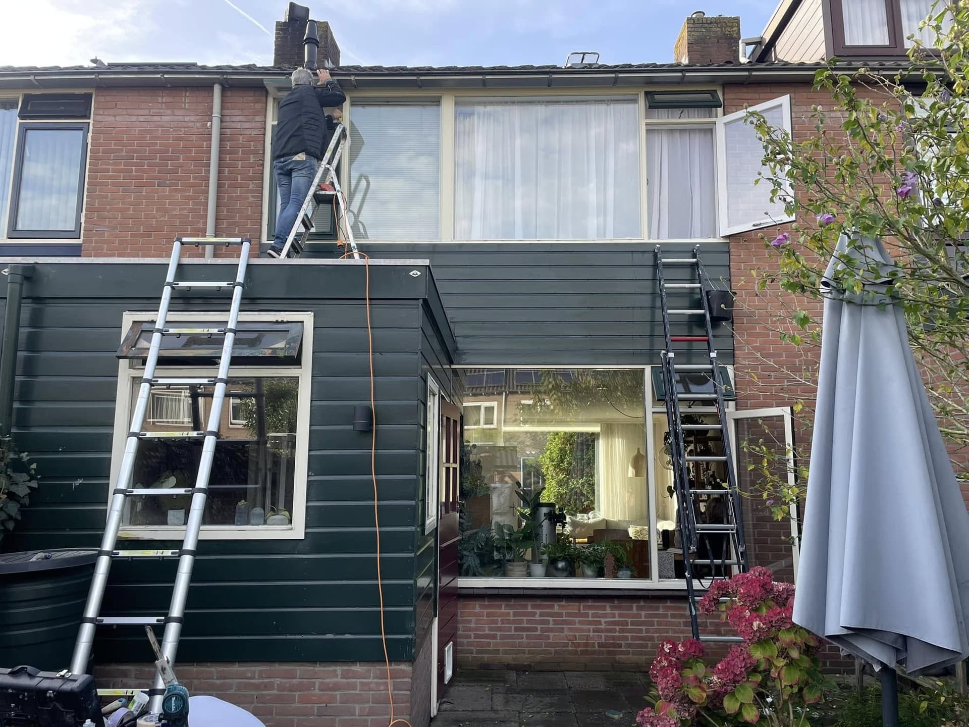 Tijdens het werk: achtergevel met twee ladders; de verdieping is al donker geschilderd. (Facebook, 16 oktober 2024)