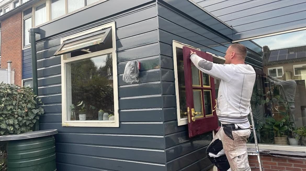 Tijdens het werk: de geschilderde bordeauxrode deur wordt teruggeplaatst naast het witte raam. (Facebook, 16 oktober 2024)